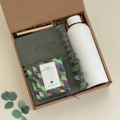 an open box containing a white bottle, notebook and green leafy paper napkins