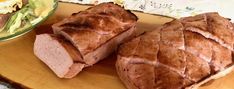 two slices of meat sitting on top of a wooden cutting board next to a salad