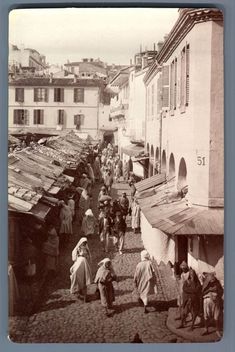 an old black and white photo of people walking down a street with buildings in the background