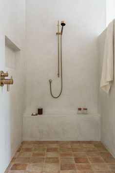 a bathroom with white walls and tile flooring has a shower head, two brass faucets, and an open window