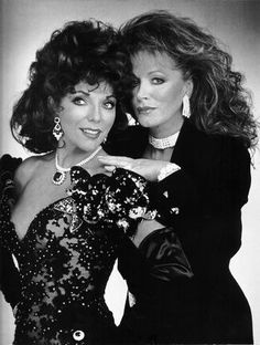 two women in black dresses posing for the camera with their hands on each other's shoulders