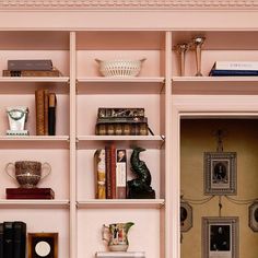 a book shelf filled with lots of books next to a wall covered in pink walls