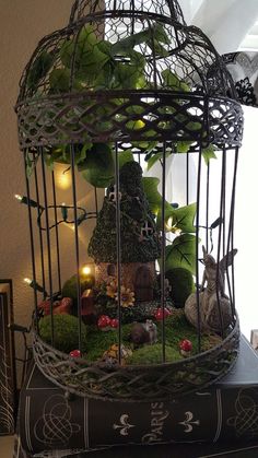 a birdcage filled with lots of plants and small animals sitting on top of a pile of books