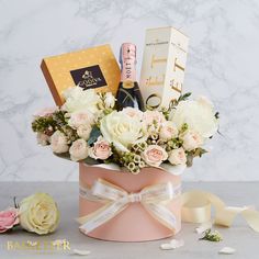 a bouquet of flowers in a pink hat box with champagne, roses and chocolates