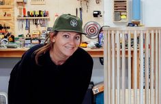 a woman wearing a green hat sitting in front of a wooden rack with tools on it