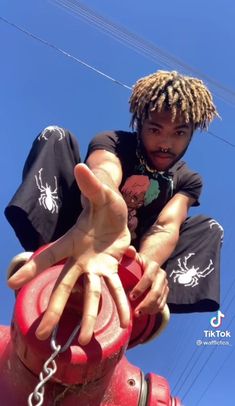 a man with dreadlocks sitting on top of a red fire hydrant