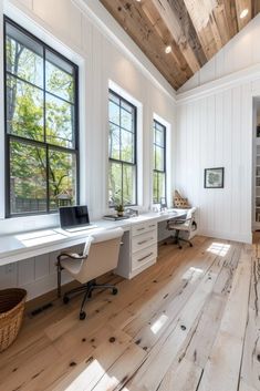 a home office with wood floors and white walls, along with two large windows that look out onto the woods