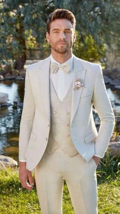 a man in a white suit and bow tie standing on the grass with his hands in his pockets