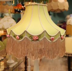 a lamp shade with flowers and fringes on it in a room filled with furniture