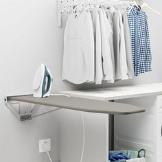 an ironing board sitting on top of a dryer next to clothes hanging in a closet