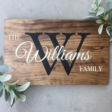 a wooden sign that says the williams family with white lettering on it and green leaves