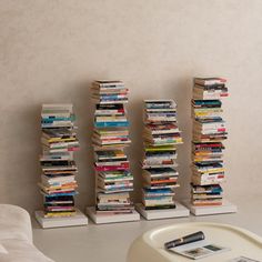 several stacks of books sitting next to each other on top of a white table in front of a wall