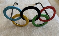 four olympic rings are sitting on a white sheet with gold, green, and blue glitter