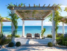 two chairs sitting under an arbor on the beach with blue water in the back ground