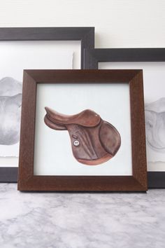 two framed pictures are sitting next to each other on a counter top, one with a horse's head painted on it