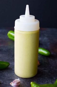 a bottle filled with mustard sitting on top of a table next to some green peppers