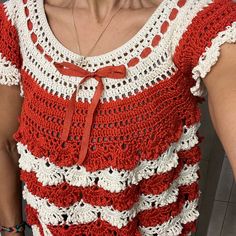 a woman wearing a red and white crocheted top with a bow tie around her neck