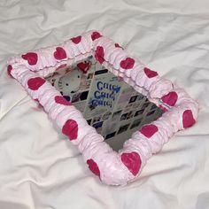 a heart shaped mirror sitting on top of a white bed covered in pink and red hearts