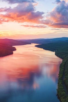 an aerial view of a lake at sunset with clouds in the sky and trees around it