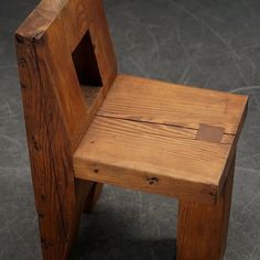 a small wooden chair sitting on top of a cement floor next to a black wall