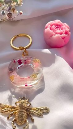 a bee keychain sitting on top of a white cloth next to a pink flower