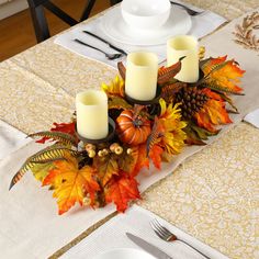 a centerpiece with candles and fall leaves on a dining room table set for thanksgiving