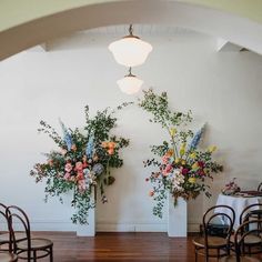 two vases filled with flowers sitting on top of a wooden floor next to chairs