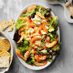 a salad with shrimp, lettuce and carrots in it next to crackers