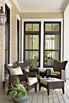 a porch with wicker furniture and potted plants on the front porch, along with two large windows