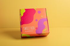 a pink box with colorful designs on the front and bottom, sitting on a yellow surface