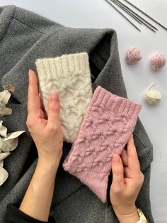 two hands holding knitted items next to knitting needles and yarns on a table