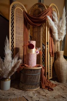 a pink cake sitting on top of a table next to some feathers and vases