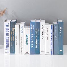 a row of blue and white books sitting on top of a table next to a vase