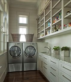 a washer and dryer in a small room with white cabinetry, wood flooring and open shelving