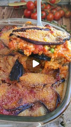 a glass dish filled with food sitting on top of a wooden table next to tomatoes