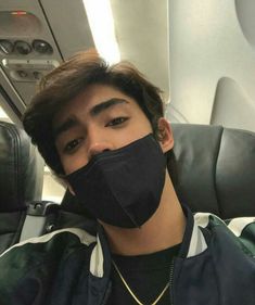 a young man wearing a black face mask on top of an airplane seat in the sun