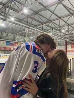 a man and woman kissing each other in front of an ice hockey jersey on the rink