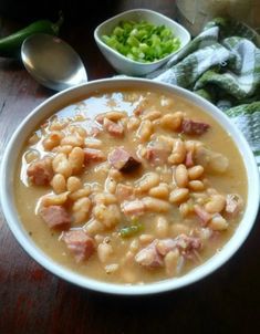 a bowl filled with beans and ham next to other dishes on a wooden table top