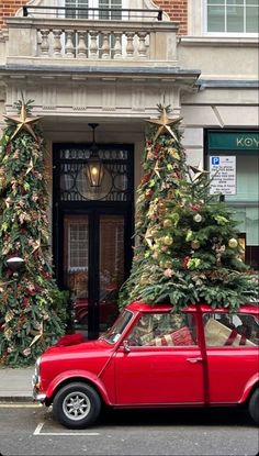 a red car parked in front of a building with christmas trees on the top and bottom