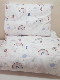 a white bed with rainbows, clouds and trees printed on the pillowcase is next to a pink wall