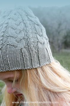 a woman with blonde hair wearing a gray knitted hat and looking at the camera