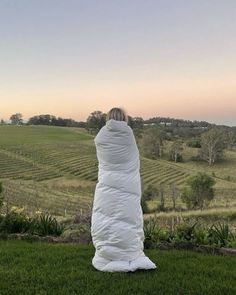 a person wrapped in a blanket sitting on top of a lush green field