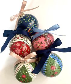 four decorated christmas balls with ribbons tied around the top one is pink, blue and green