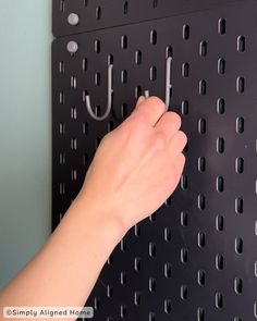 a person's hand is holding an umbrella hook on a pegboard with holes in it