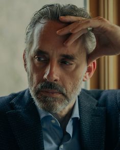 a man in a suit and tie holding his hand to his head while looking at the camera