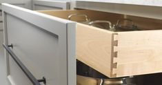 an open drawer in a kitchen with pots and pans on the bottom shelf,