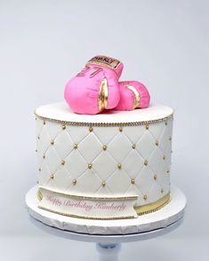 a birthday cake with two pink boxing gloves on it's top and gold trimmings