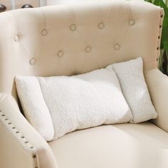 a white chair with two pillows on it and a plant in the backgroud