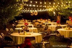 an outdoor event with tables and chairs covered in white tablecloths, lit by string lights