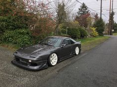 a black sports car parked on the side of a road next to bushes and trees